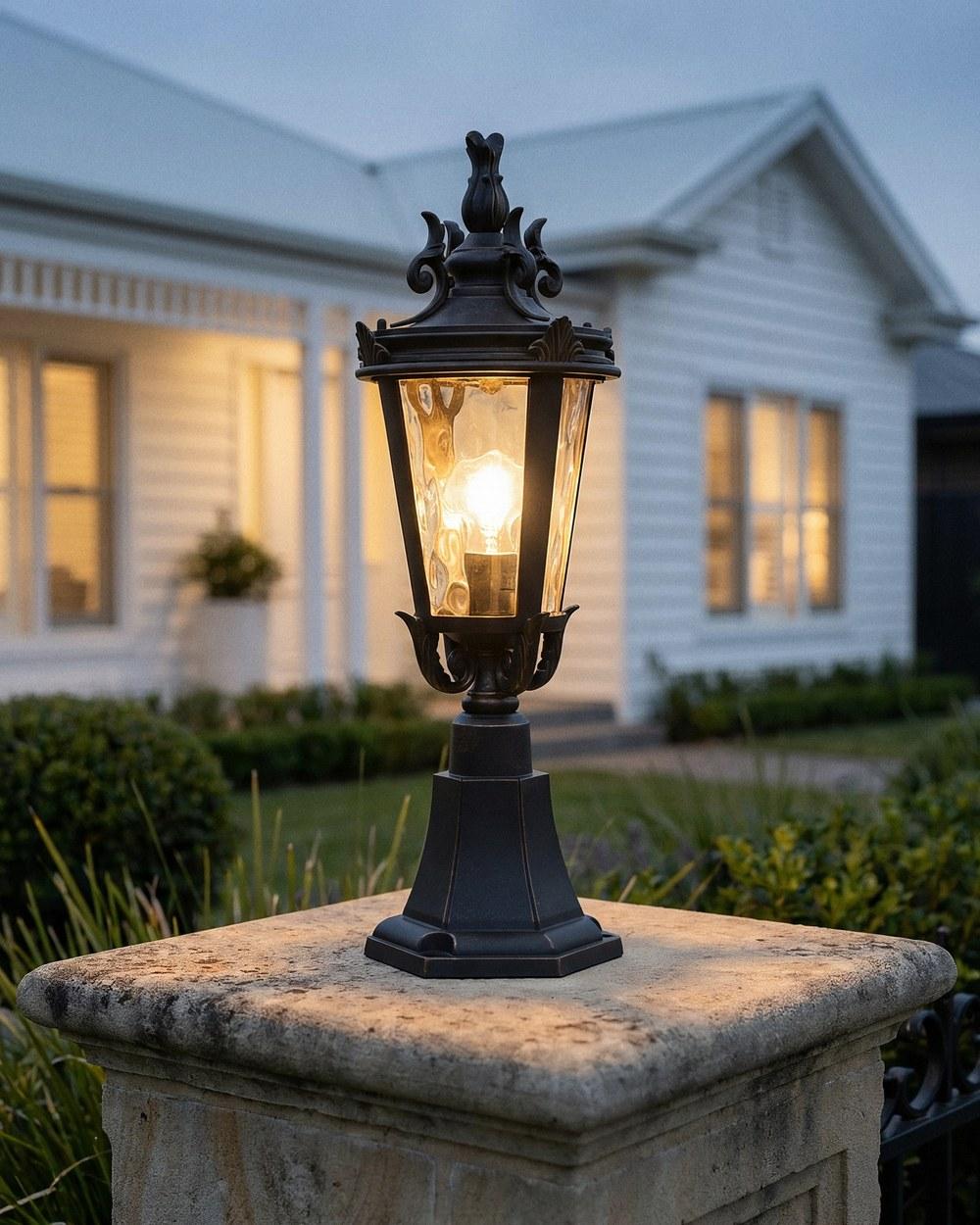 Albany outdoor pillar mount in antique bronze lit on a stone pier outside a weatherboard home